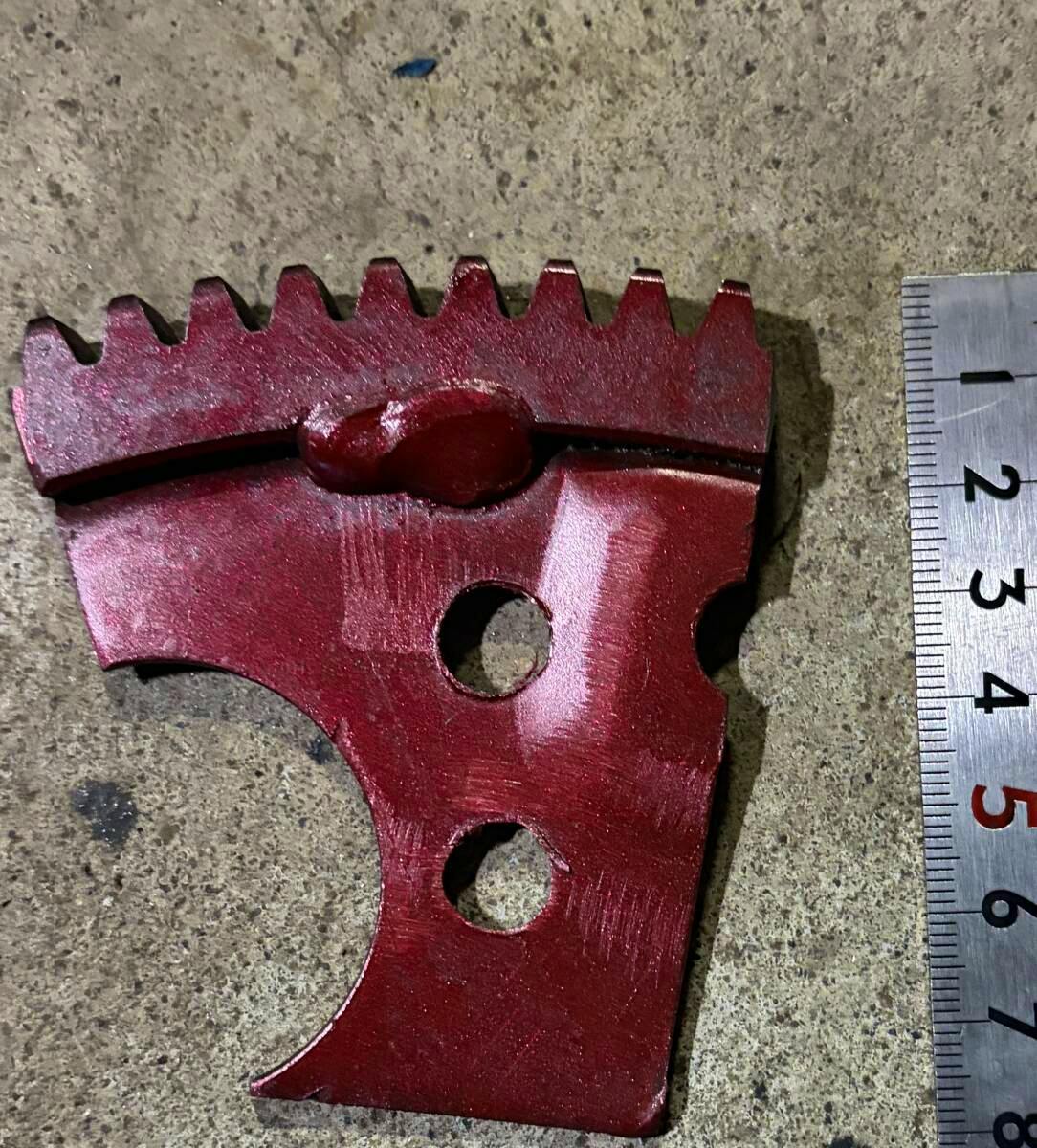 Red metal flywheel stopper tool photographed on a concrete surface with a ruler alongside to show scale.