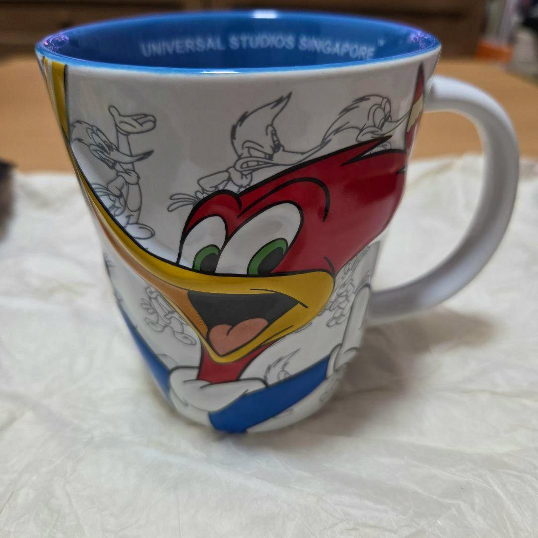 A ceramic Woody Woodpecker mug showing a close-up of Woody's colorful face, white handle, and blue interior rim.