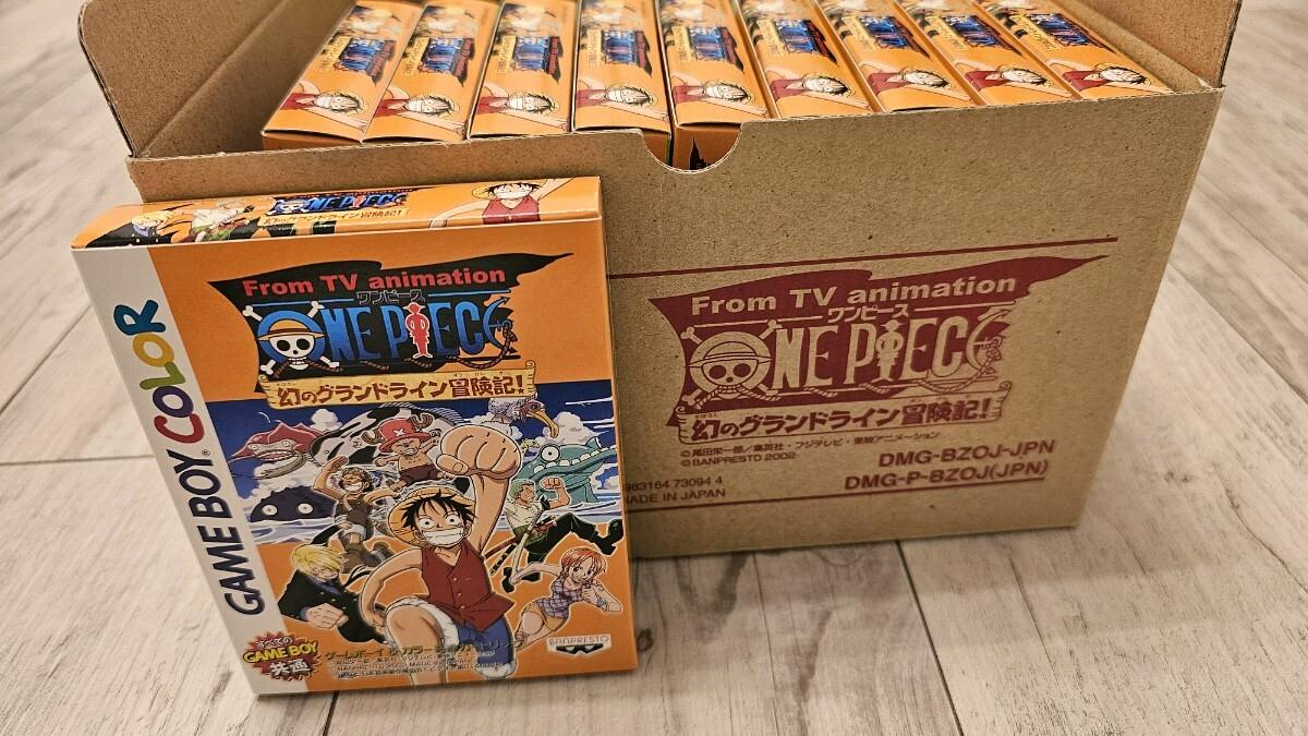 Multiple unopened Game Boy Color ONE PIECE game boxes arranged inside a cardboard carton with one box shown in front on a wooden floor.