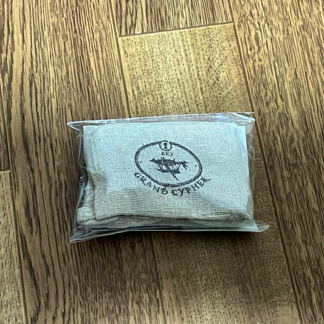 Unopened packaged fabric pouch keyholder showing a printed logo on the front, lying on a wooden floor.
