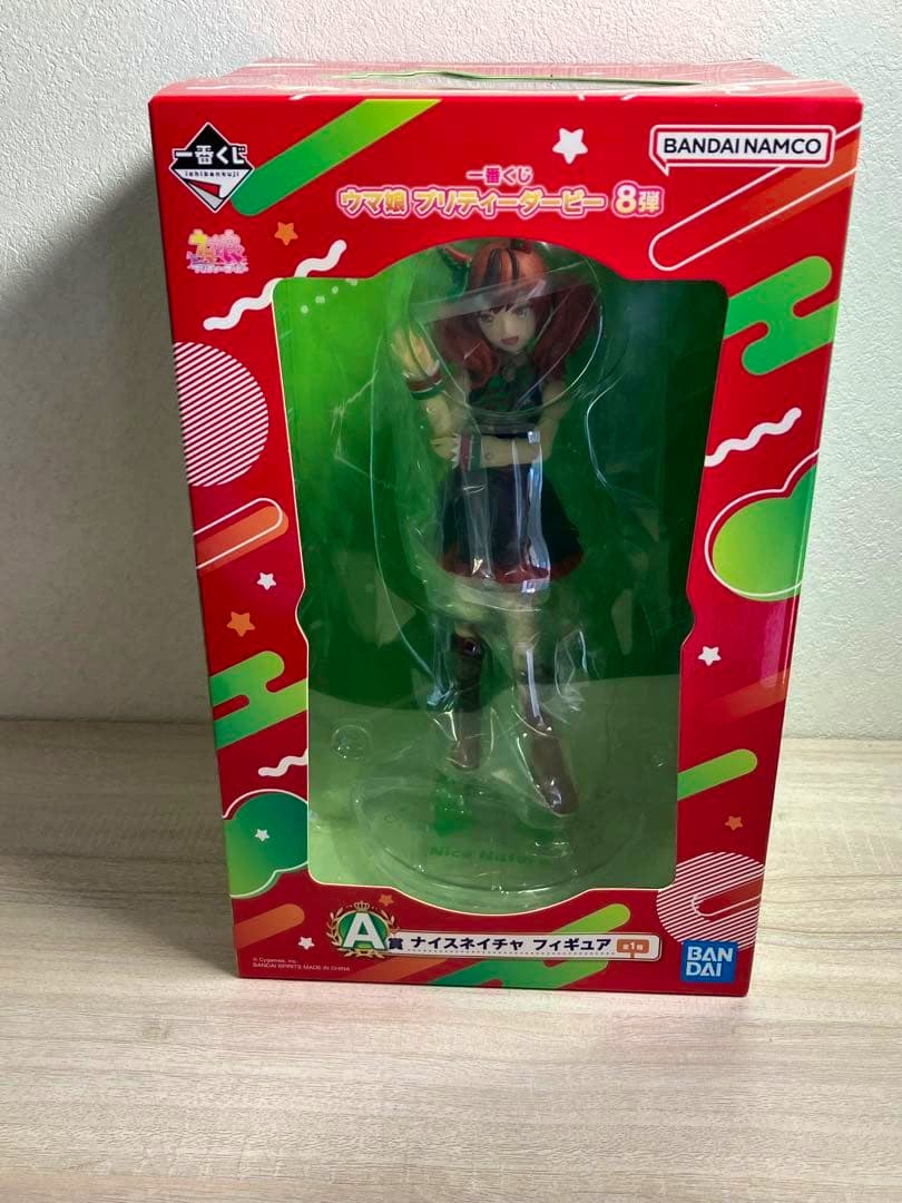 Front view of the boxed Nice Nature A‑prize figure from Uma Musume Pretty Derby visible through the red and green Bandai Namco packaging window.