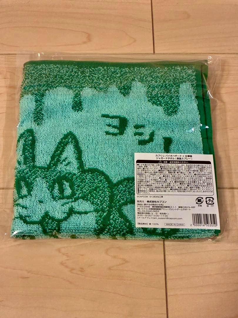 Folded green jacquard towel with a cat design sealed in plastic packaging with a product information sticker visible.