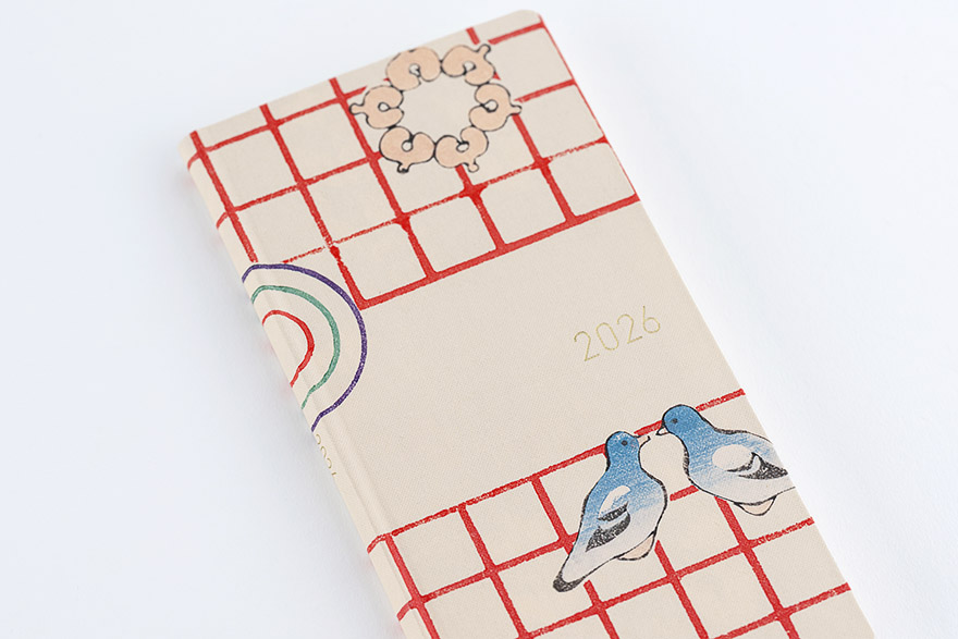 Hardcover weekly horizontal notebook with a cream cover decorated with a red grid, two blue pigeons, decorative motifs, and the year 2026 printed.