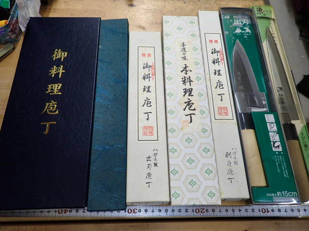 Several boxed Japanese chef knives arranged side by side on a table with some blades visible and a measuring ruler along the bottom.