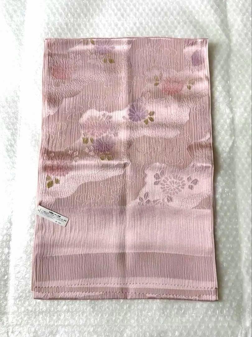 Pink silk obiage (帯揚げ) laid flat showing a subtle floral woven pattern and a small tag.