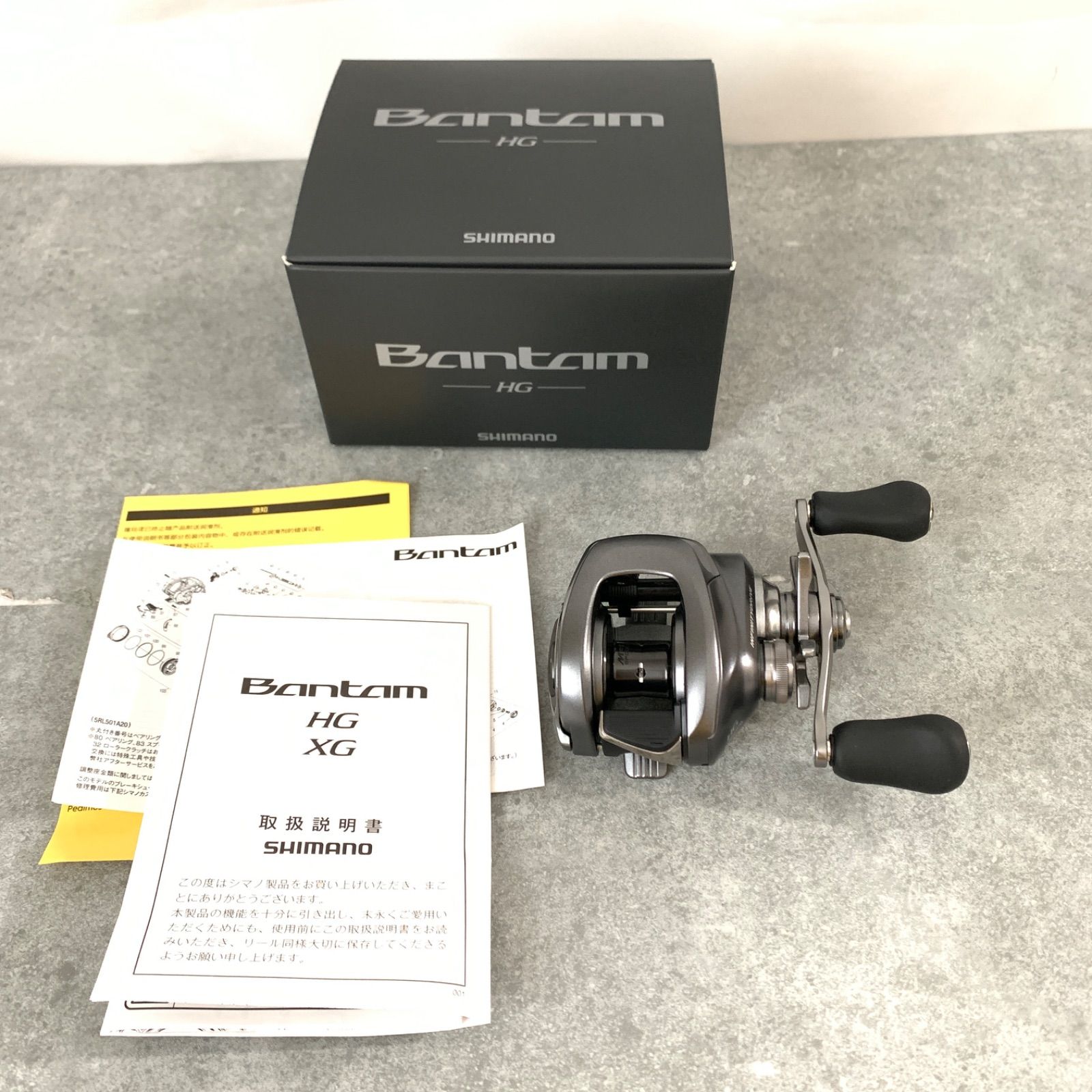 Shimano Bantam baitcasting fishing reel with its box and manuals on a gray surface.