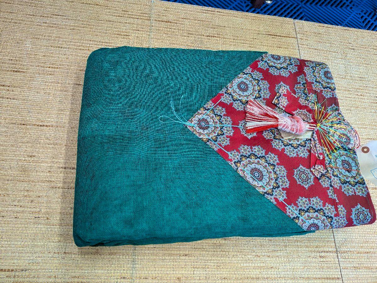 Folded green hemp mosquito net with a red patterned corner and tassel on a woven mat.