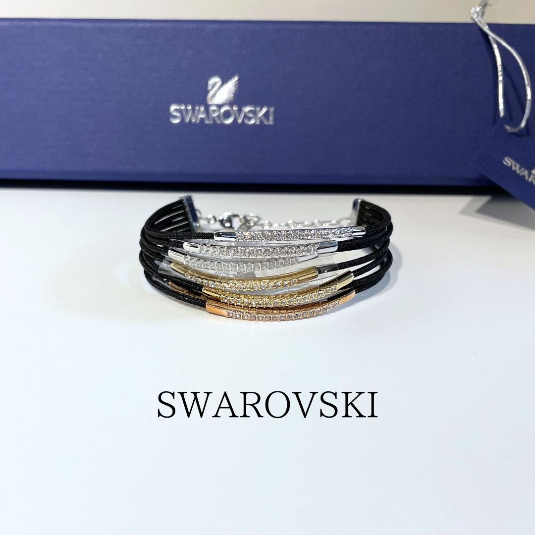 Multi-strand black cord bracelet with crystal-studded metal bars displayed in front of a blue Swarovski box.