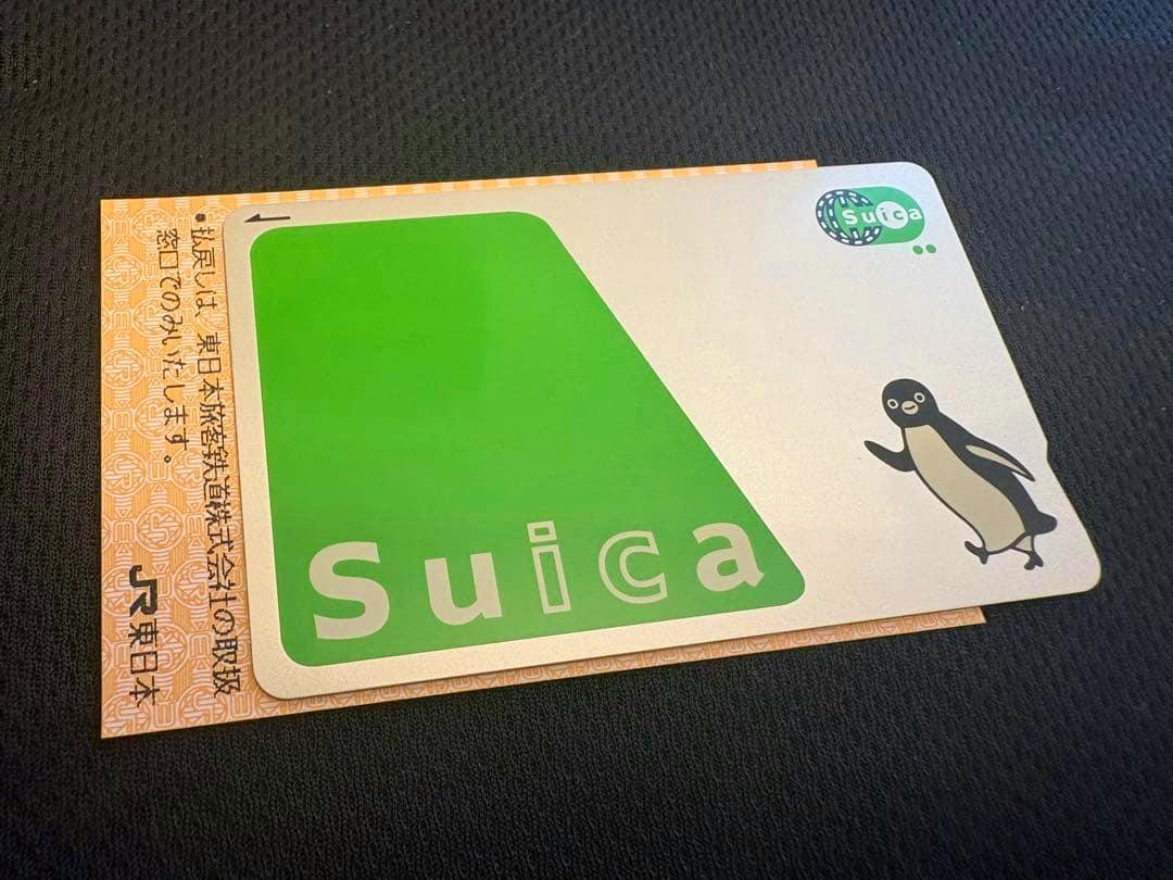 Photograph of a Suica plastic card showing the green Suica logo and penguin design on a dark fabric background.