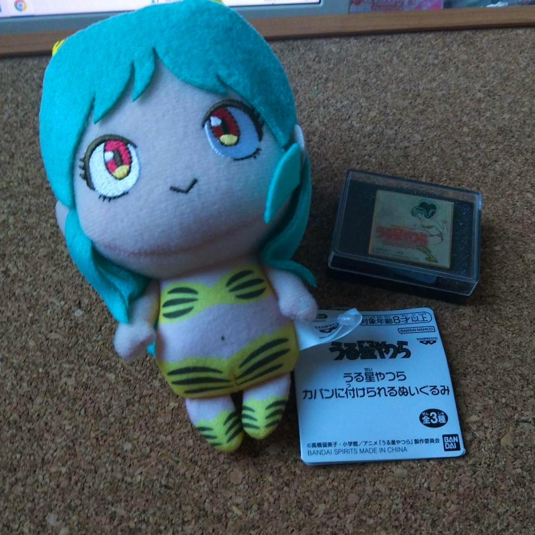 Front view of the うる星やつら plush in bikini style with teal hair and a yellow-striped bikini on a corkboard next to its tag and a small plastic case.