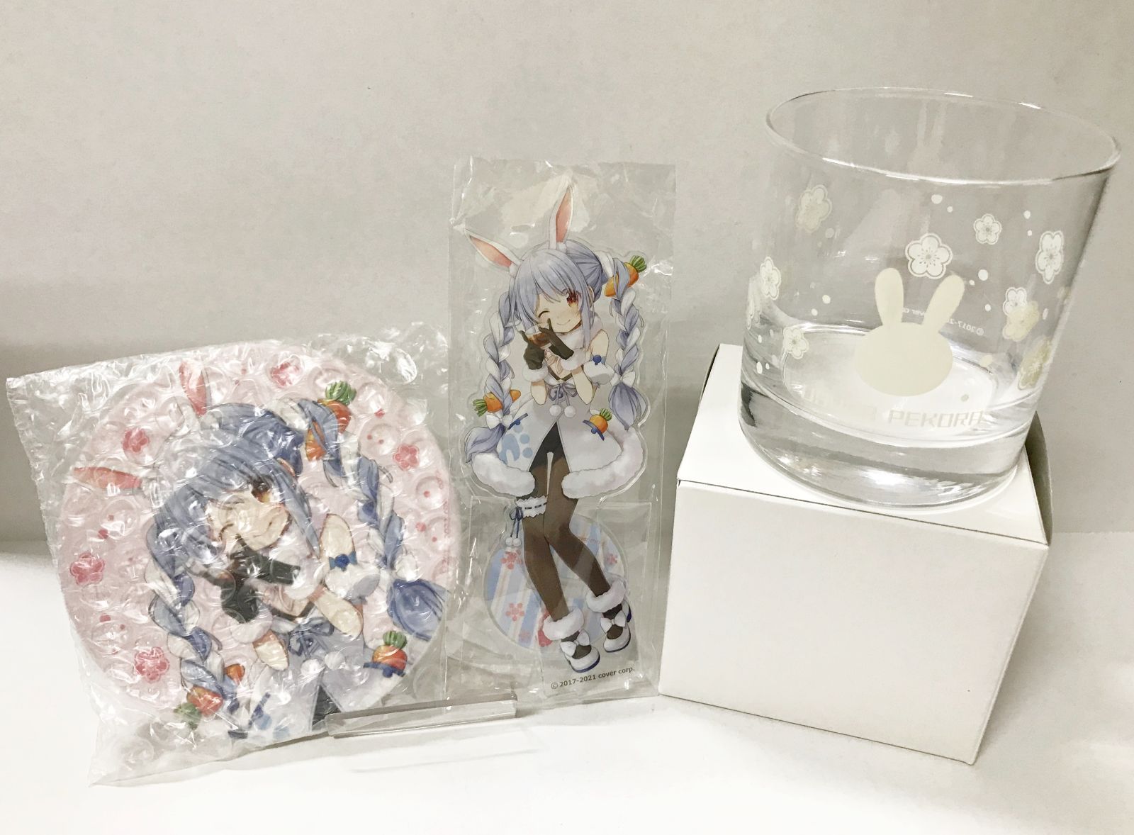 Clear drinking glass with a white bunny motif next to two sealed character acrylic goods on a white background.