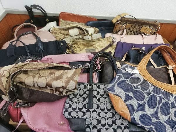 A pile of assorted used bags, including several Coach handbags, arranged together on a surface.