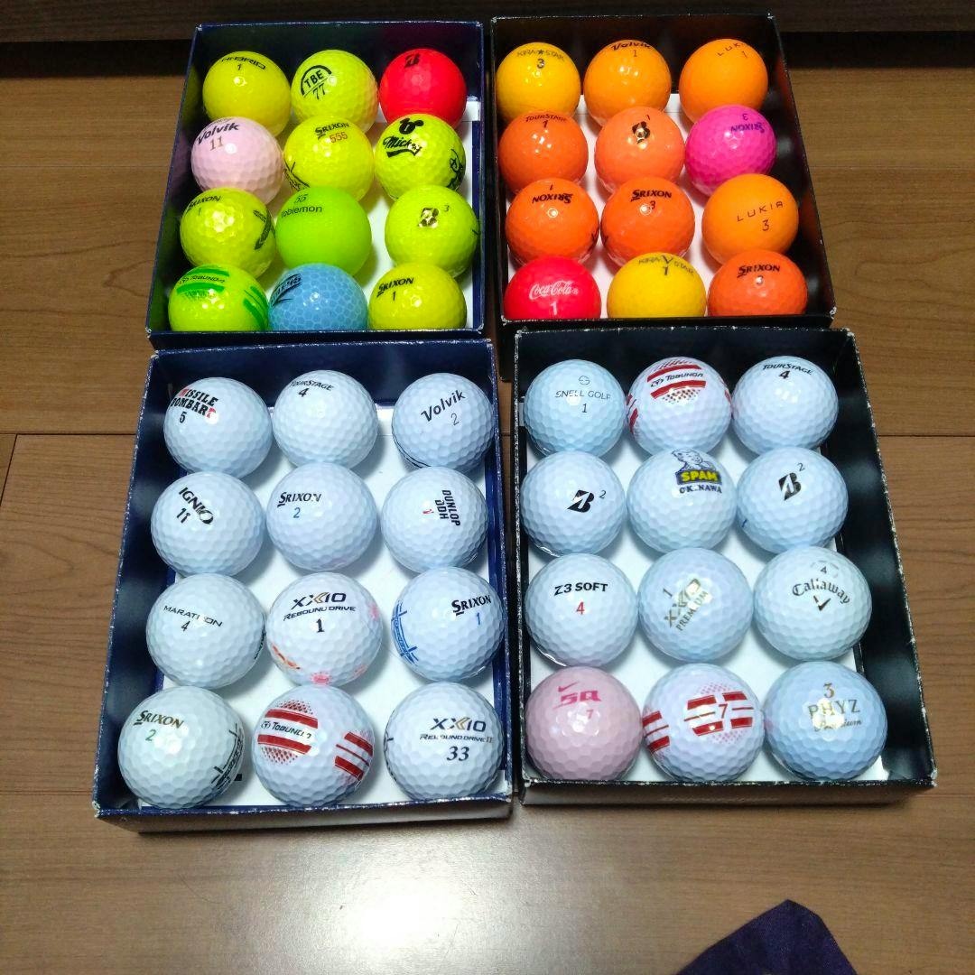 Four trays filled with mixed-color and white golf balls arranged in rows on a wooden floor.