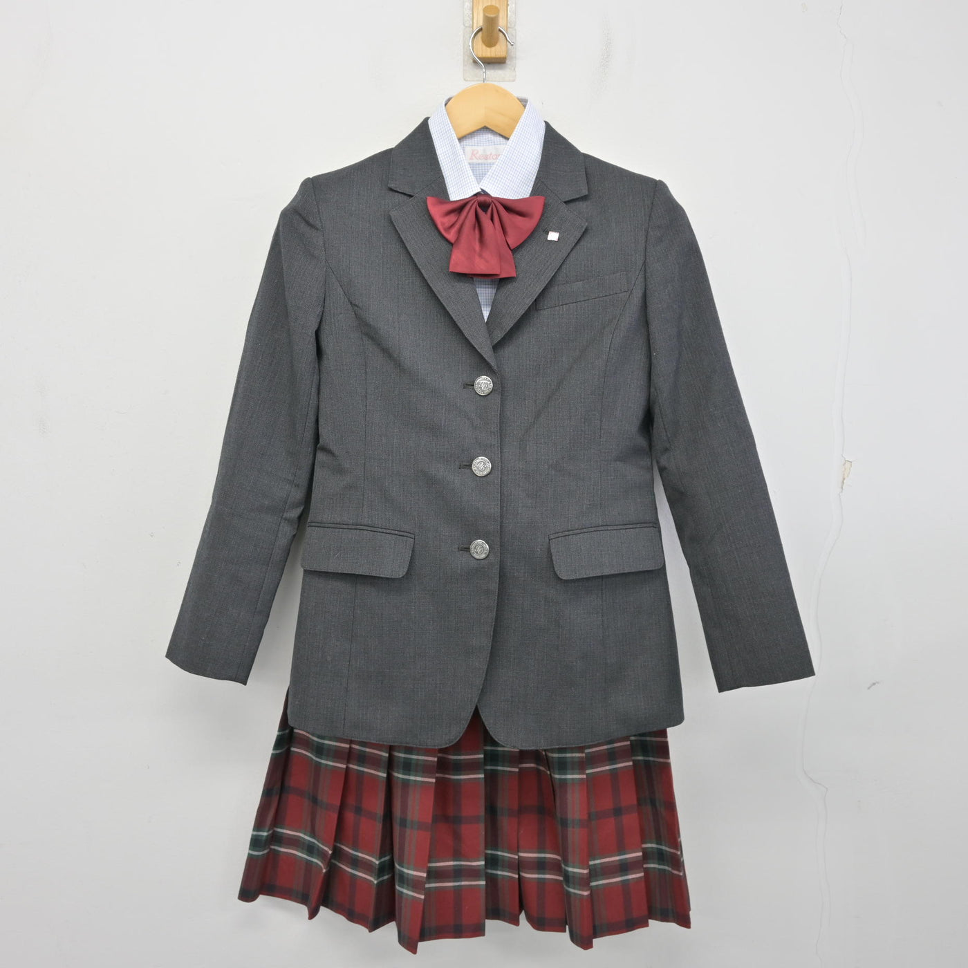 Gray girls' school blazer with white shirt, red bow, and red plaid skirt displayed on a hanger against a white background.