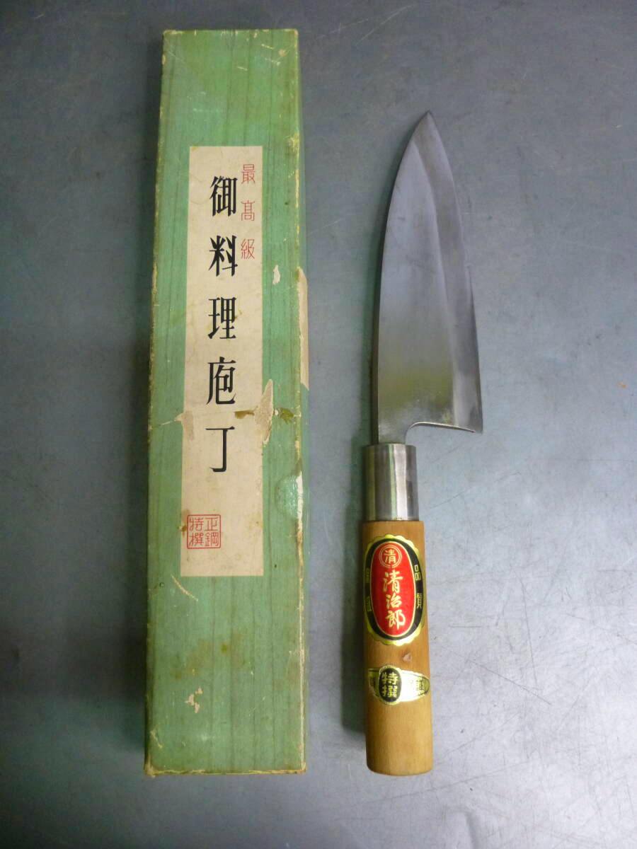 A used deba-style chef knife with wooden handle and metal collar displayed next to a green box.