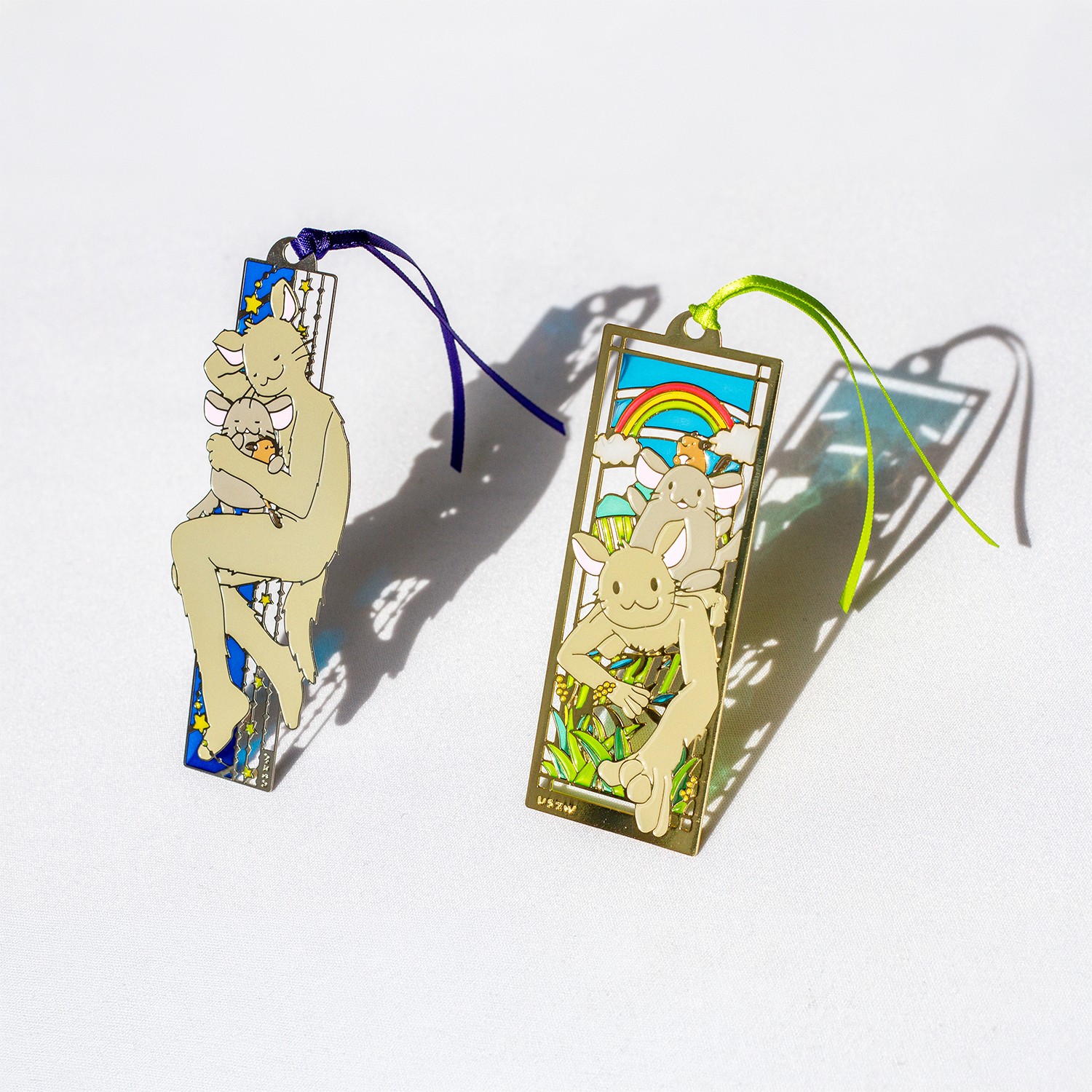 Photo of two rectangular stained-glass-style bookmarks featuring rabbit characters with attached ribbons on a white surface.