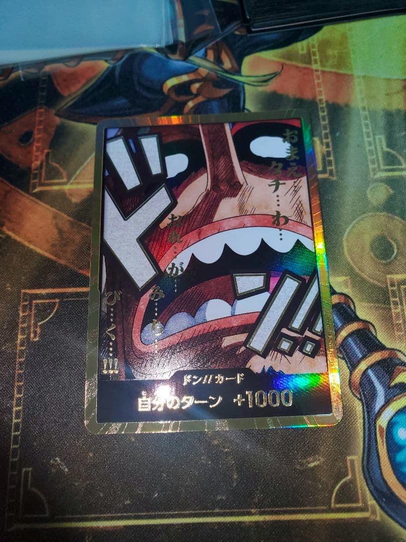 Front of the ウソップ 金ドン trading card showing a manga-style close-up of a mouth with large Japanese sound-effect text and a holographic gold border.