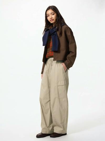 Female model wearing beige utility volume pants with side cargo pockets, standing against a white background.