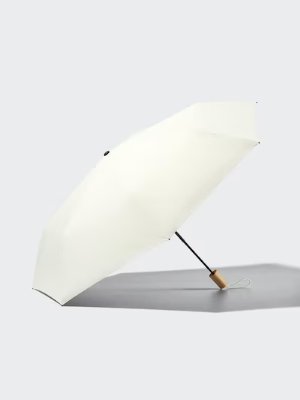 A compact umbrella (UV-blocking) with a light-colored canopy, black shaft, and wooden handle shown open and resting on a light background.