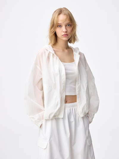 A woman modeling a white UV-cut sheer parka worn over a white crop top and white pants.