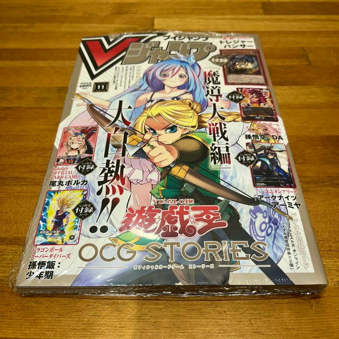 Sealed copy of Vジャンプ magazine (2025 November issue) on a wooden surface showing the illustrated cover with characters and the text “OCG STORIES.”