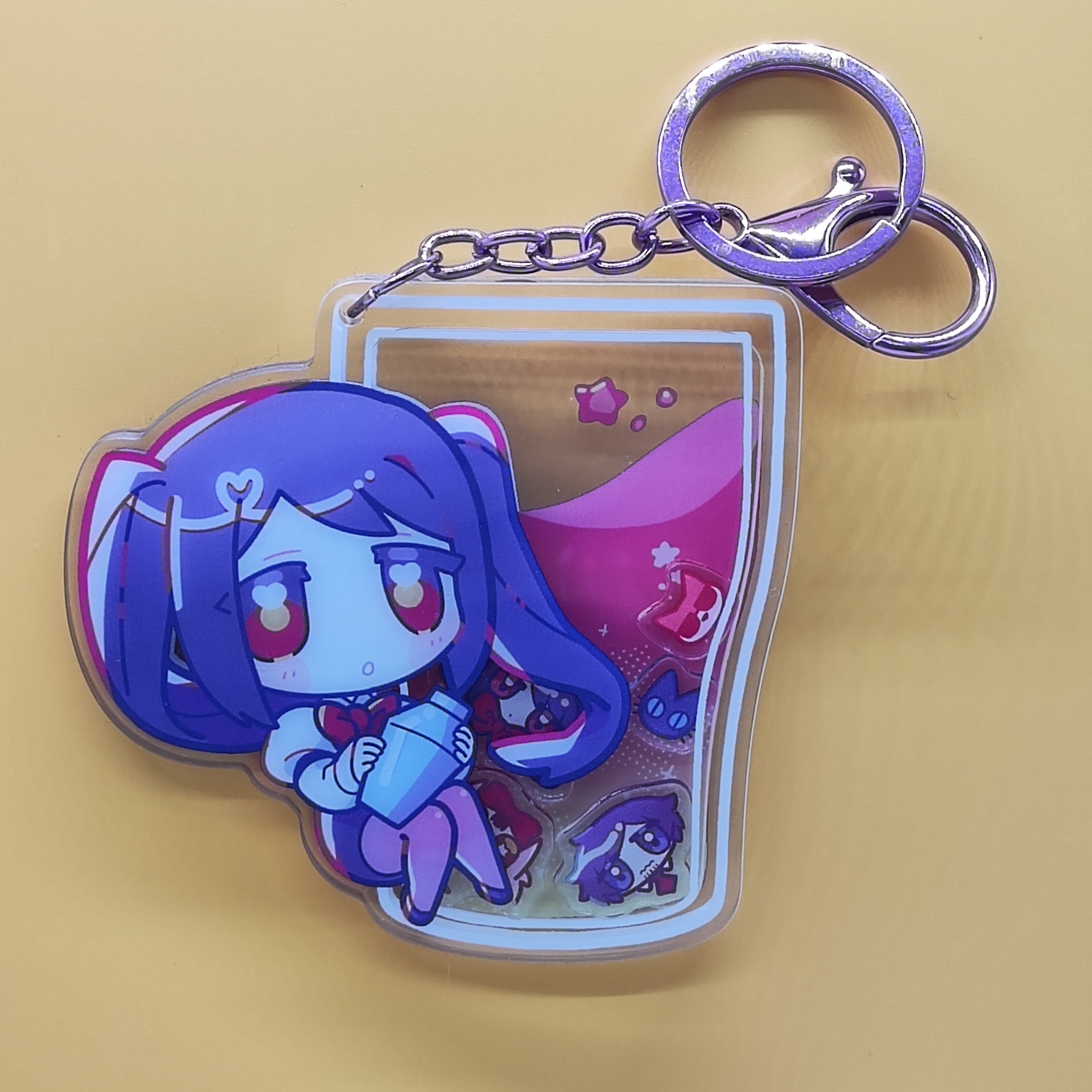 Photograph of the VA-11 Hall-A acrylic keychain with chibi character art and metal key ring on a plain yellow background.