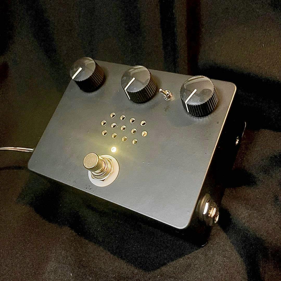 Black bass preamp guitar pedal showing three control knobs, a footswitch, and a pattern of ventilation holes on its top surface.