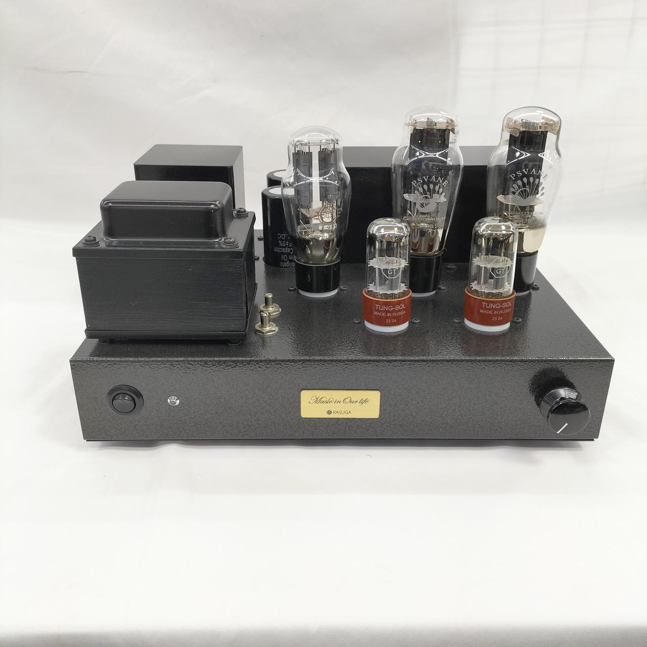 Front view of a vacuum tube power amplifier on a metal chassis showing vacuum tubes, transformer housings, a volume knob, and a power switch.