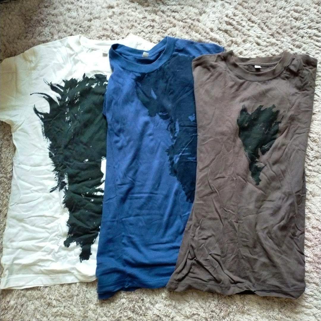 Three cotton T-shirts laid flat on a carpet (white, blue, brown), each showing a black ink-style face print.