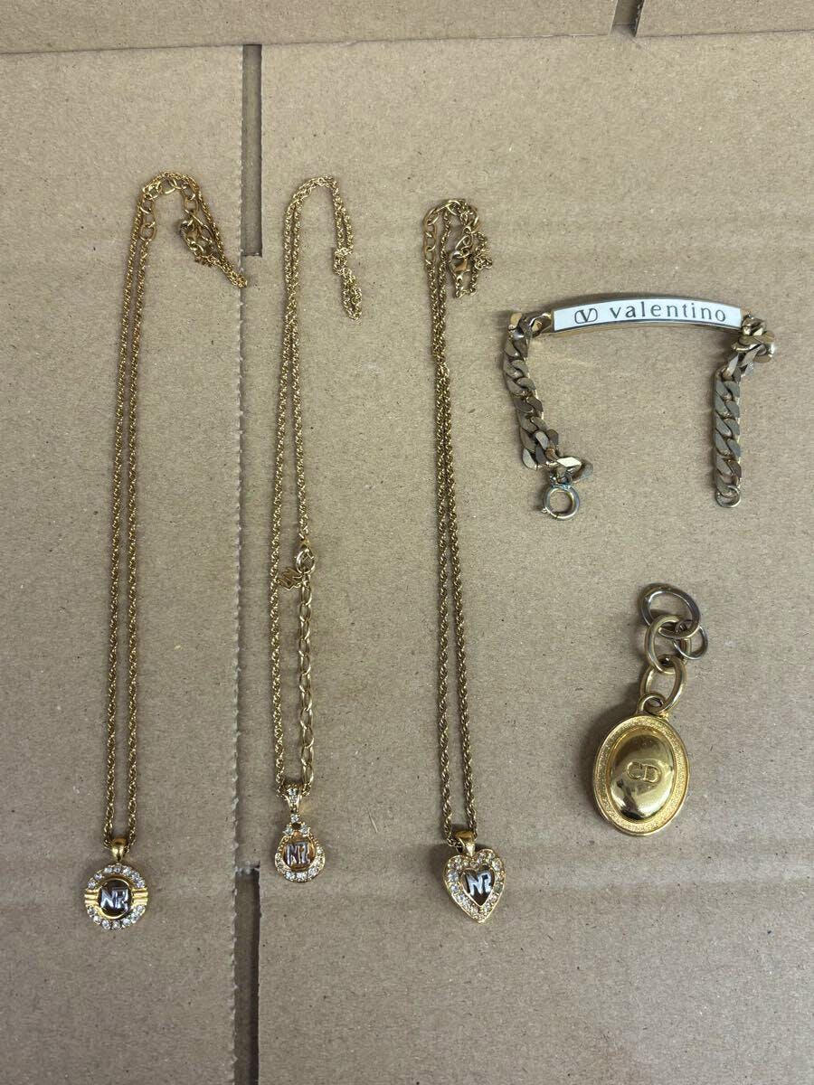 Five gold-color jewelry pieces laid on cardboard: three necklaces with round and heart rhinestone pendants, a Valentino bracelet, and a gold oval charm.