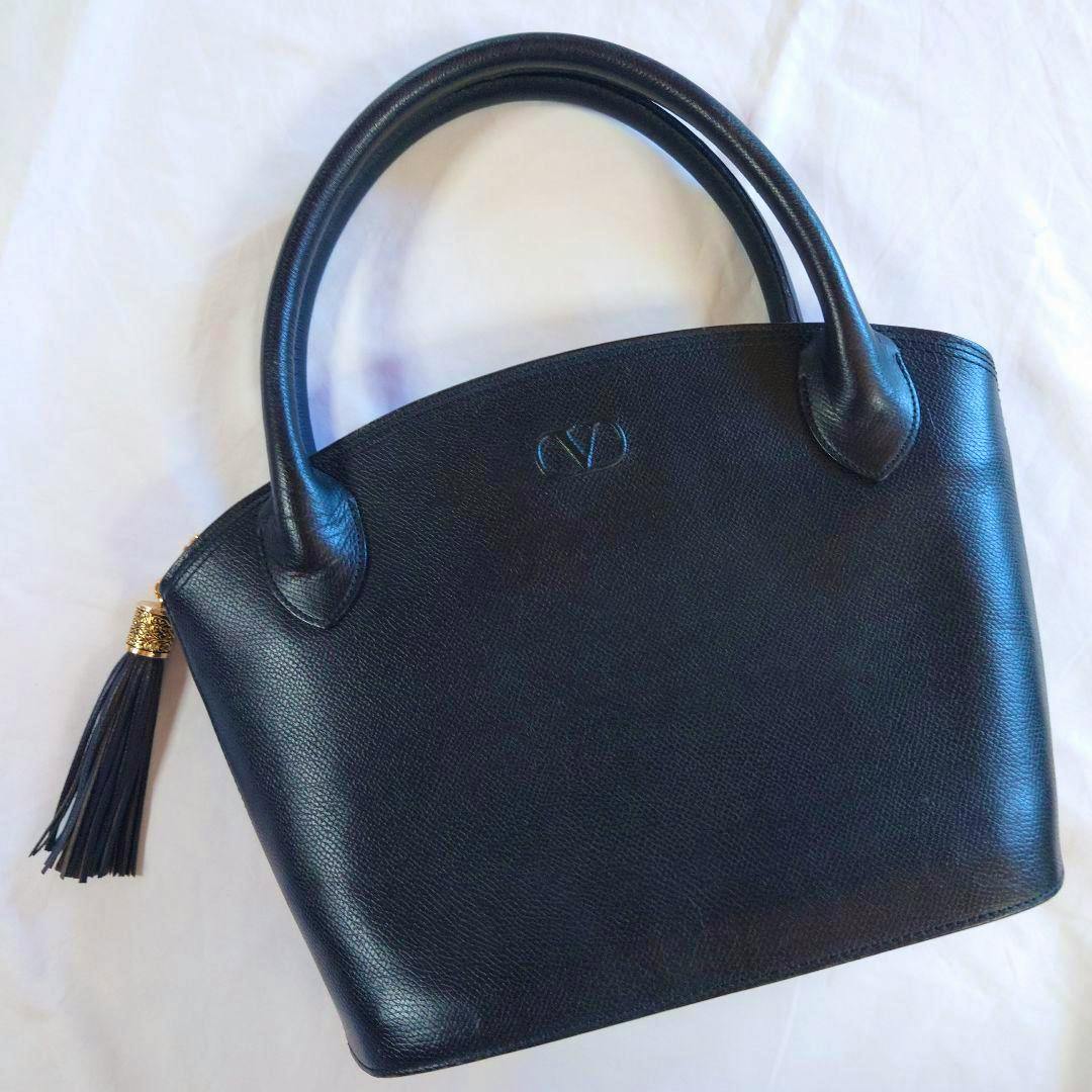 Front view of the black VALENTINO GARAVANI handbag with dual handles and a tassel, on a white background.