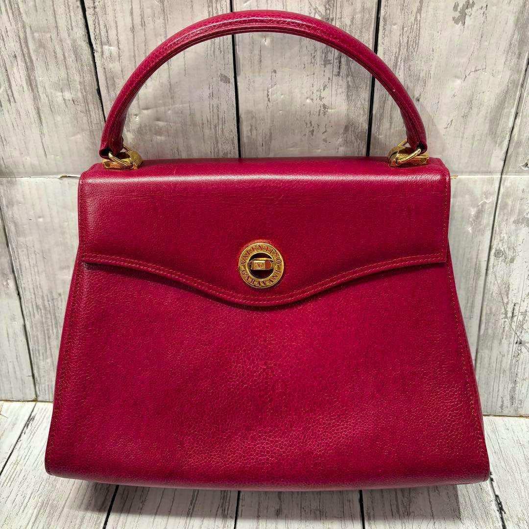 Front view of a red Valentino Garavani cow leather handbag with a top handle and a round gold turn-lock on the flap.