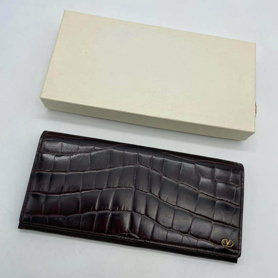 Dark brown croc-embossed long wallet shown with a cream-colored box above it.