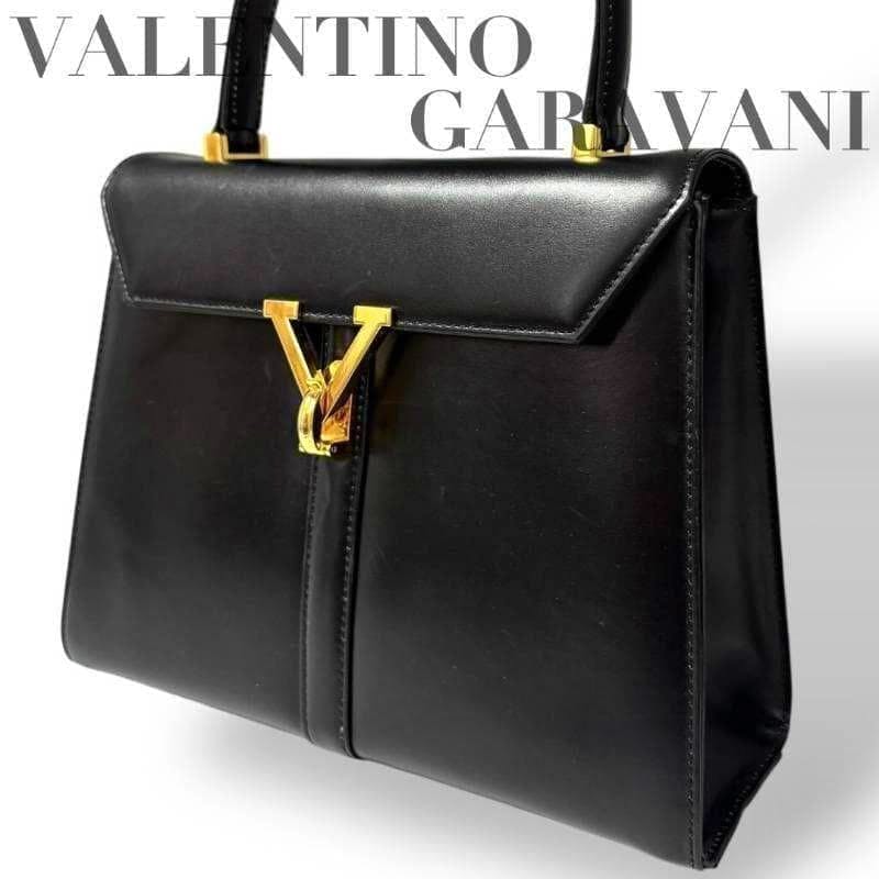 Black Valentino Garavani one-handle leather handbag with a gold V clasp on a white background.