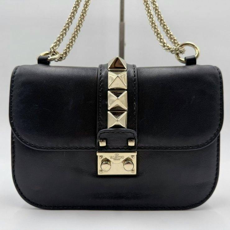 Front view of a black VALENTINO Rockstud leather shoulder bag with gold pyramid studs, gold clasp, and gold chain strap.