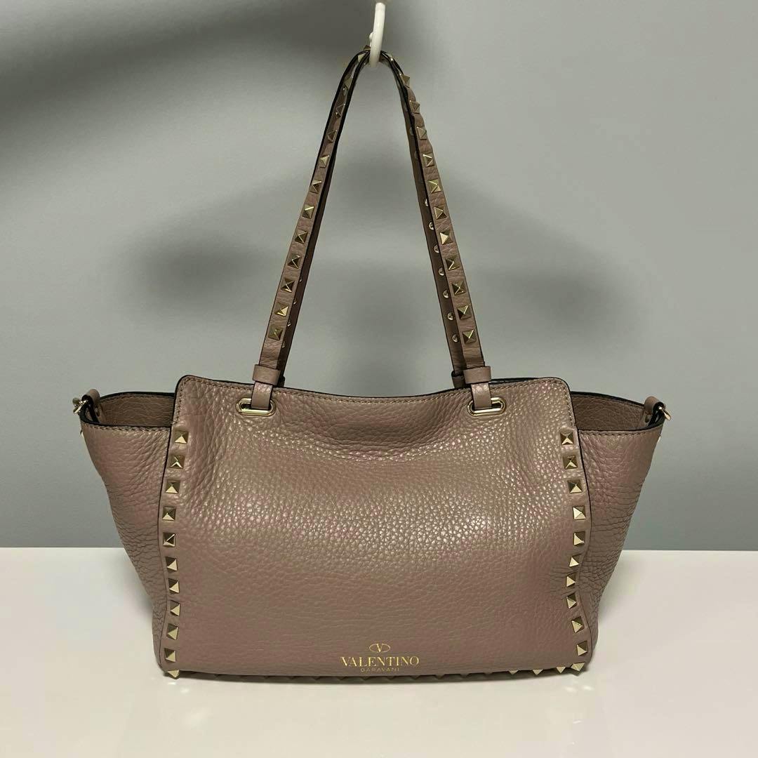 Front view of a powder-colored Valentino Rockstuds tote bag with studded straps and gold Valentino logo.