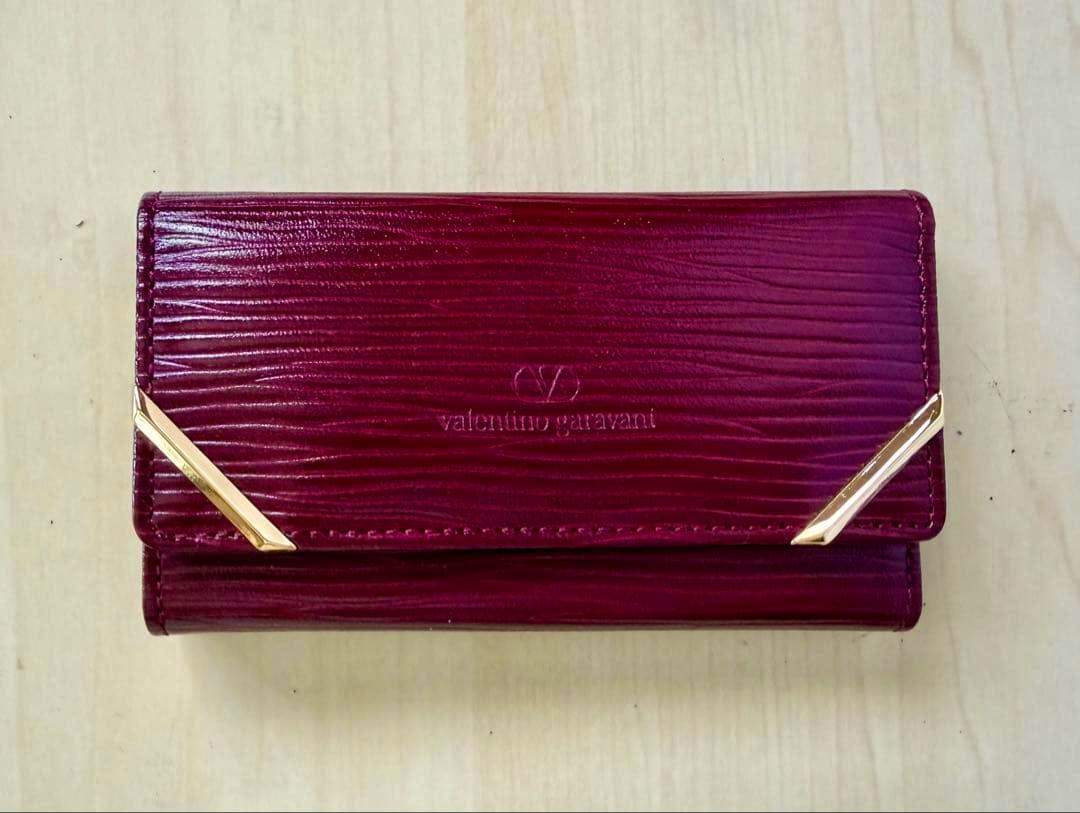 Red Valentino Garavani leather key case with gold corner accents photographed closed on a light wooden surface.