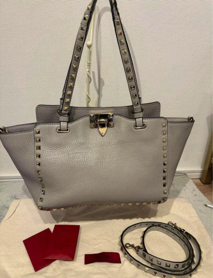 Front view of a gray Valentino Rockstud leather 2-way shoulder bag with studded handles and a detachable strap.