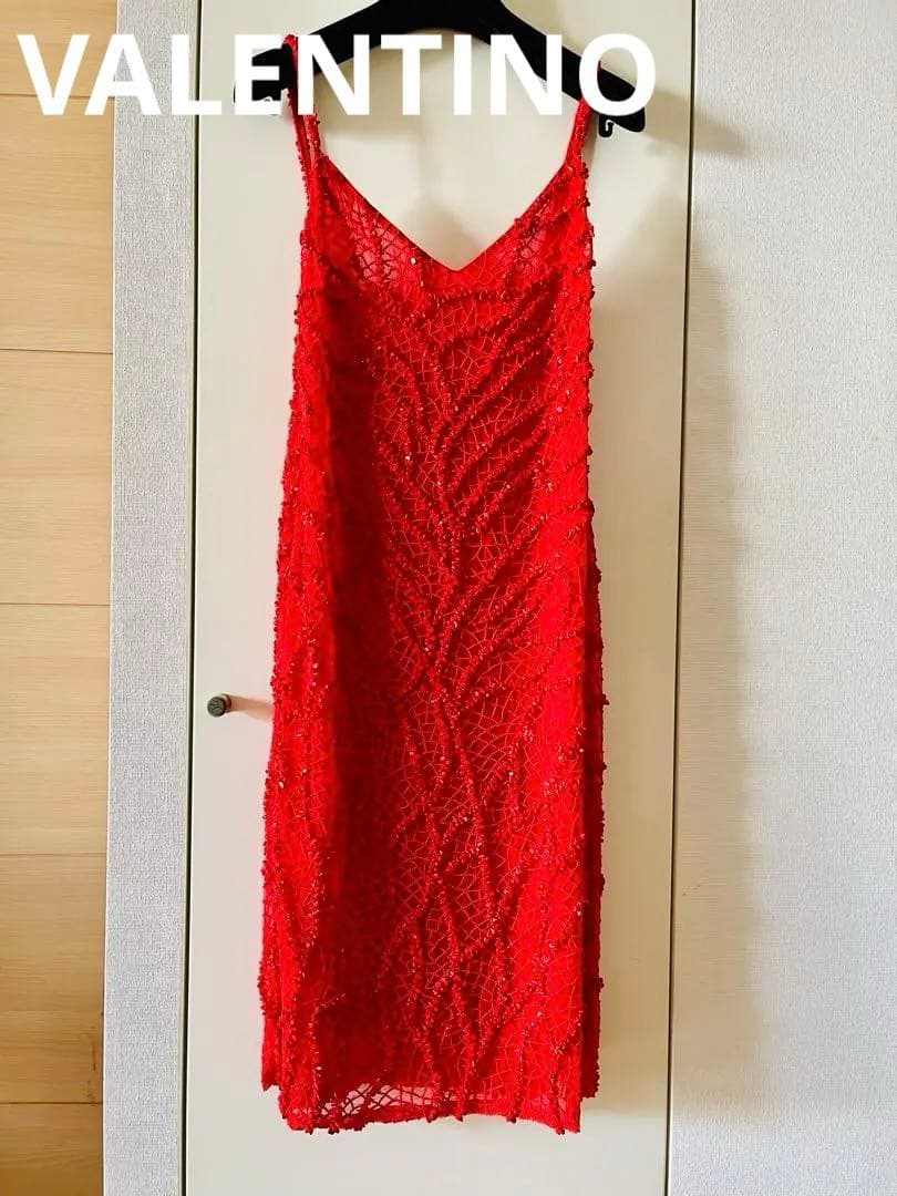 Red silk knee-length Valentino dress covered in beads hanging on a hanger against a door.