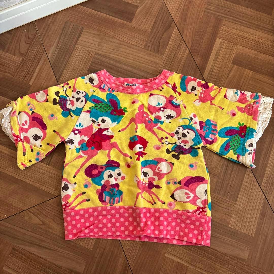 Front view flat-lay of a children's colorful T-shirt with yellow cartoon print and a pink polka-dot hem.