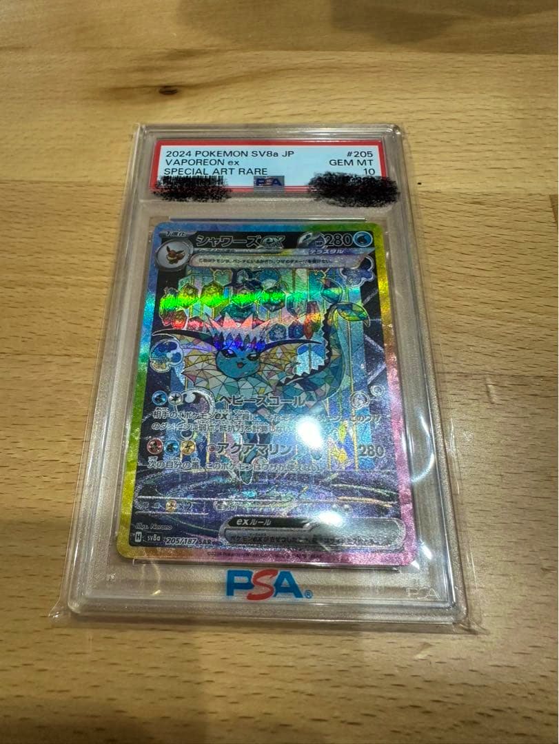 Front of the PSA-graded シャワーズex (Vaporeon ex) trading card in a clear plastic slab on a wooden table.