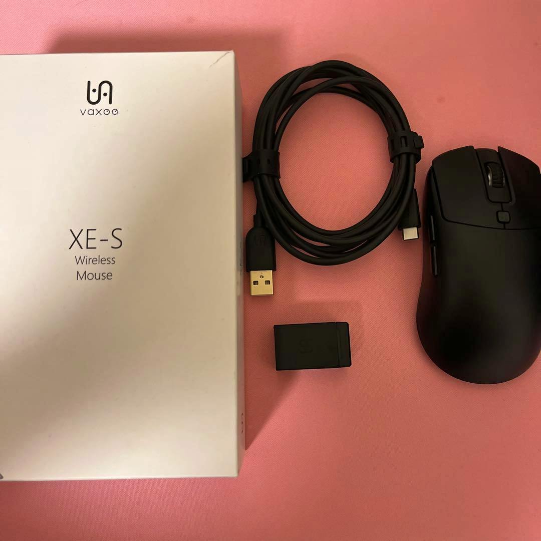 Vaxee XE-S gaming mouse shown with its USB cable, wireless receiver, and product box on a pink background.