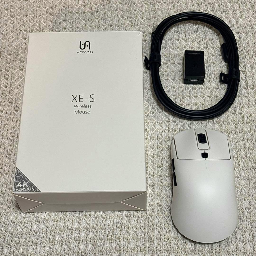 White VAXEE XE-S W wireless mouse shown with its box, USB receiver, and cable on a textured surface.