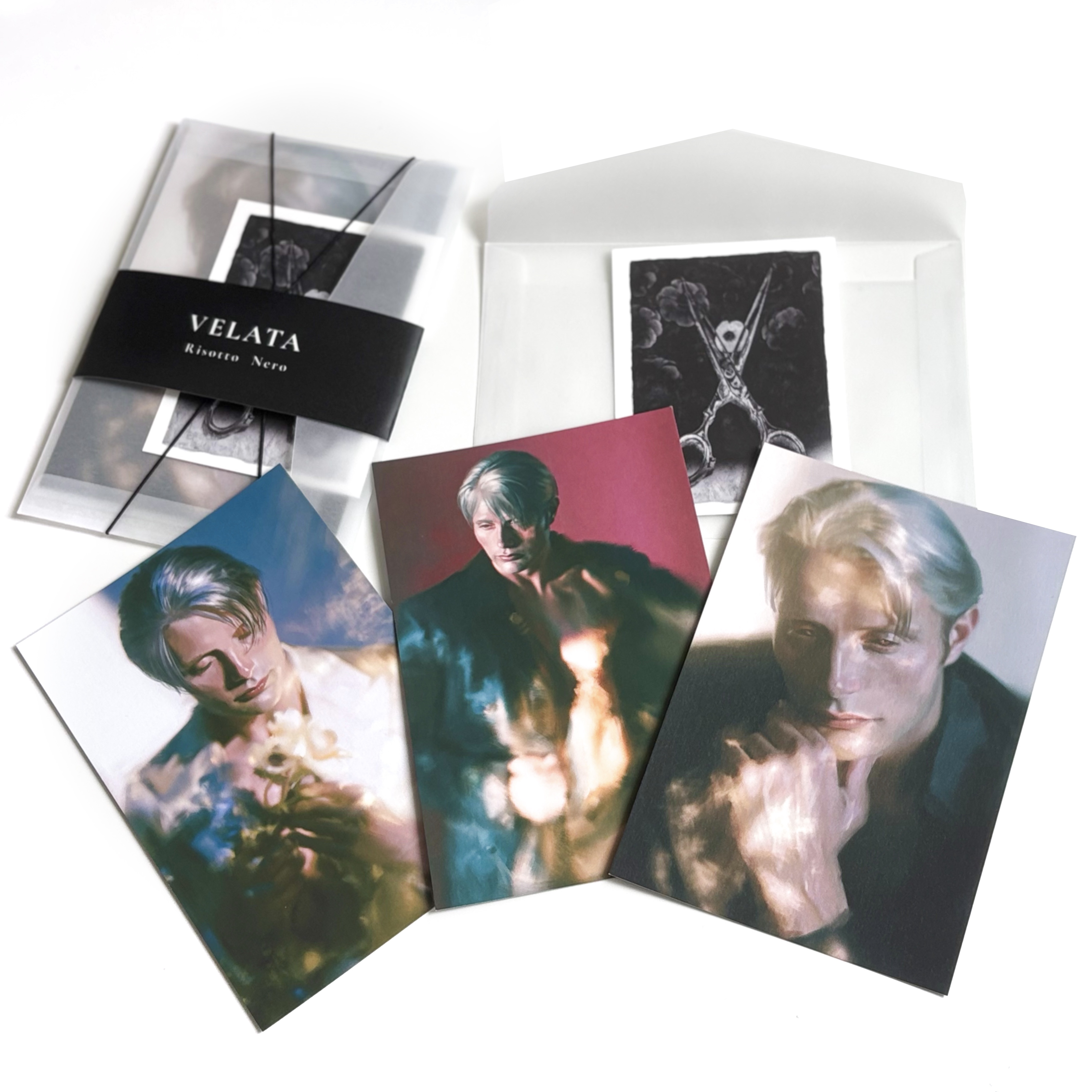 Photo of three VELATA art postcards displayed in front of their clear plastic packaging and a white envelope with a black insert.