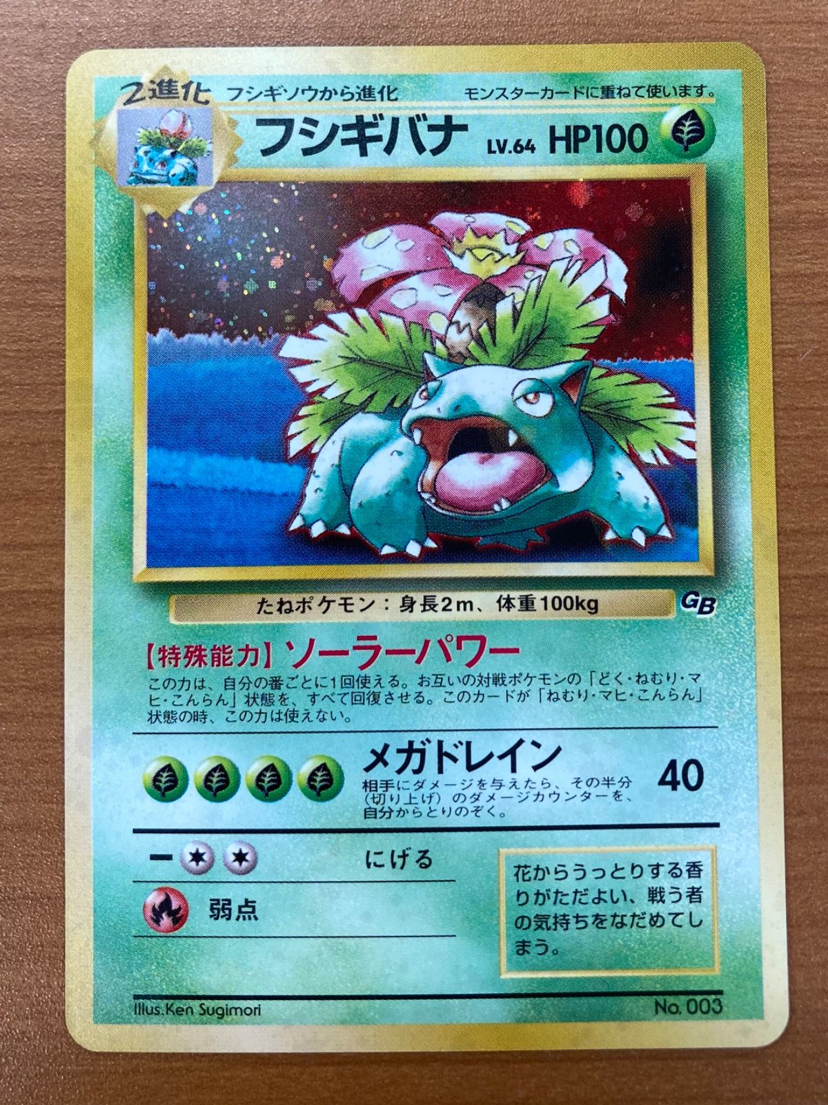 Photograph of a Japanese Venusaur (フシギバナ) trading card showing Lv.64, HP100, and ソーラーパワー text with holographic art.