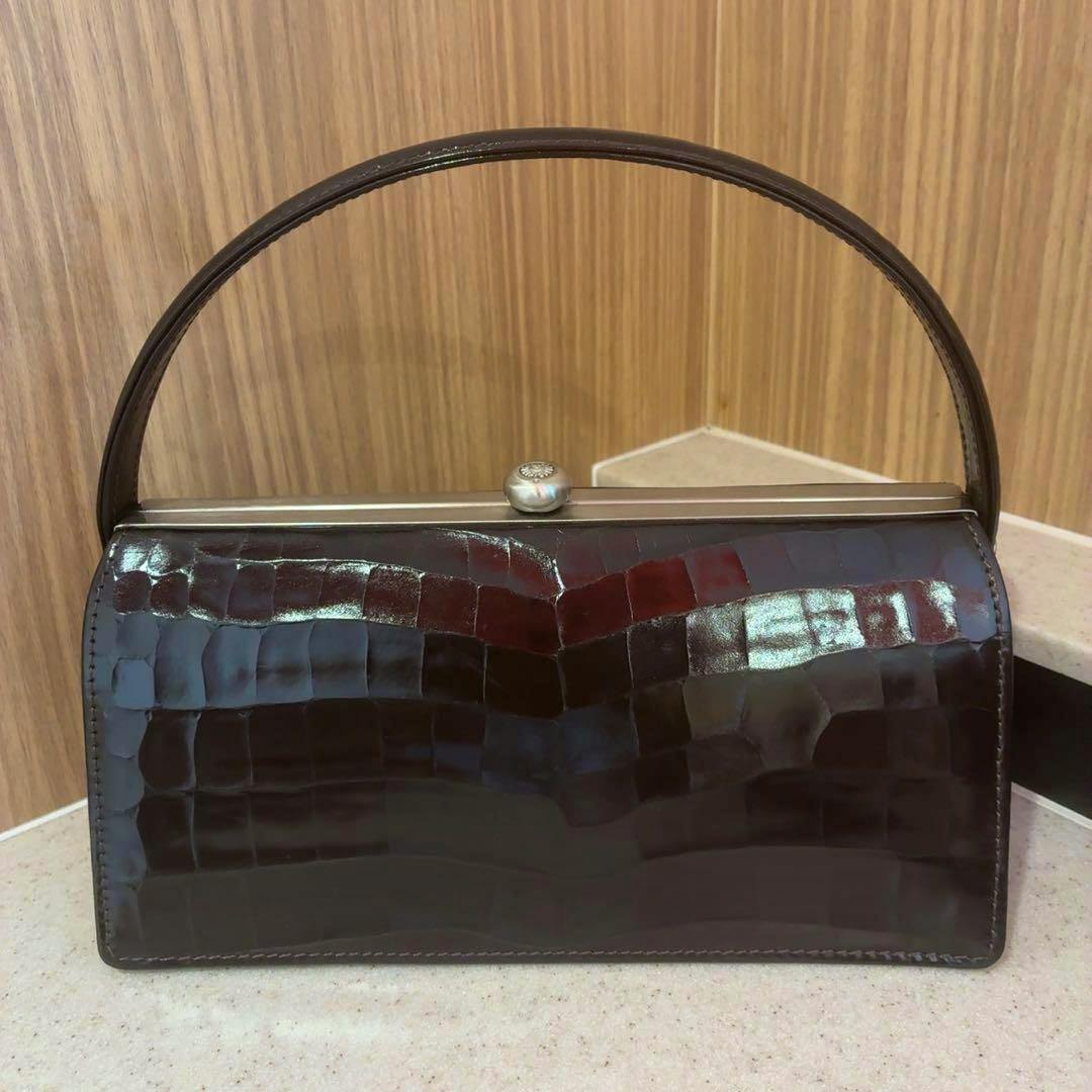 Brown crocodile-embossed clasp handbag with a single top handle shown against a wood background.