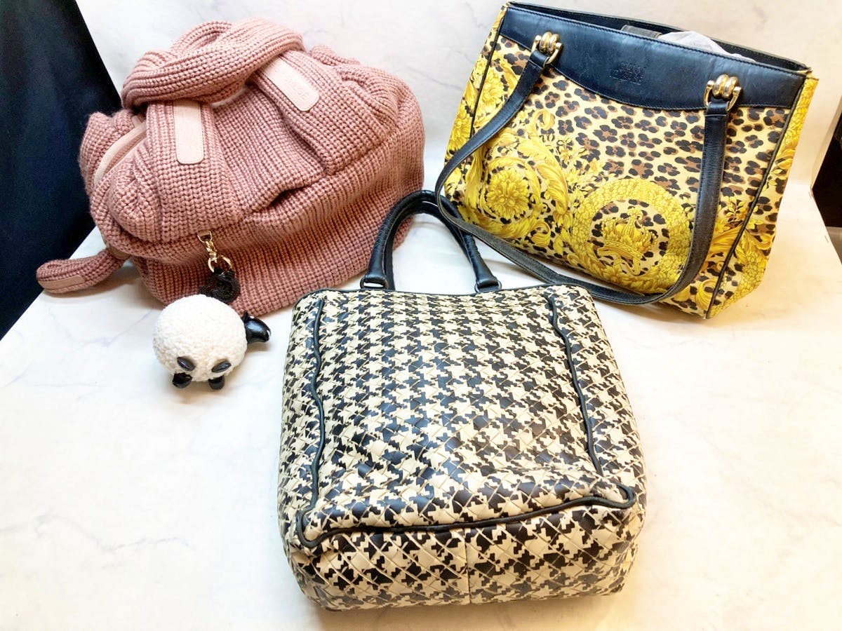 Three women's bags displayed together: a pink knitted bag with a round pom-pom charm, a black-and-white houndstooth bag, and a yellow patterned tote.