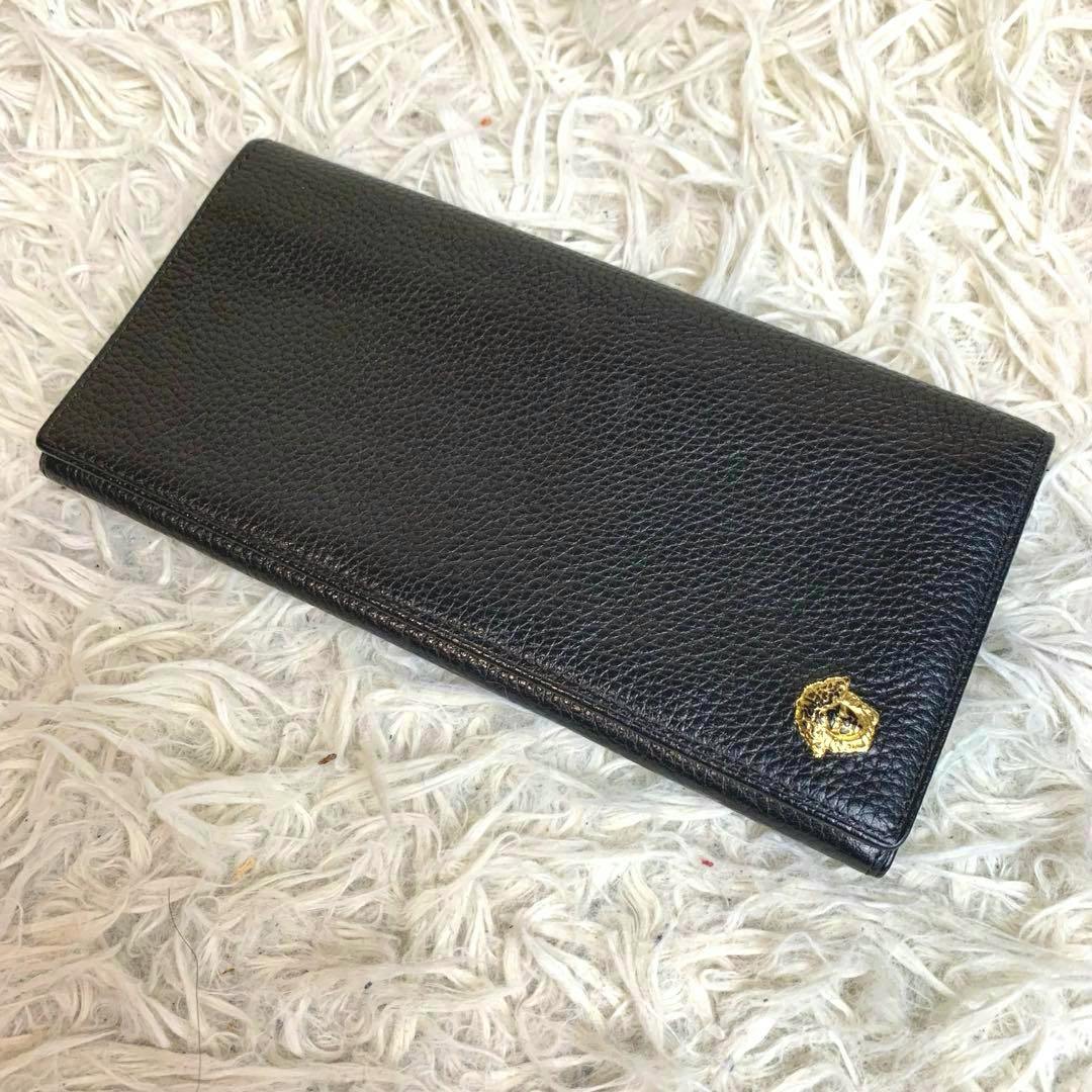 Black long leather Versace wallet with a gold Medusa emblem lying on a white shaggy rug.