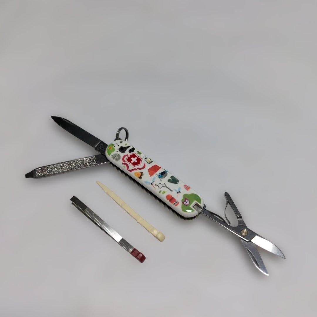 Victorinox Classic pocket knife with a decorative handle showing an open blade and scissors, with tweezers and a toothpick placed beside it.