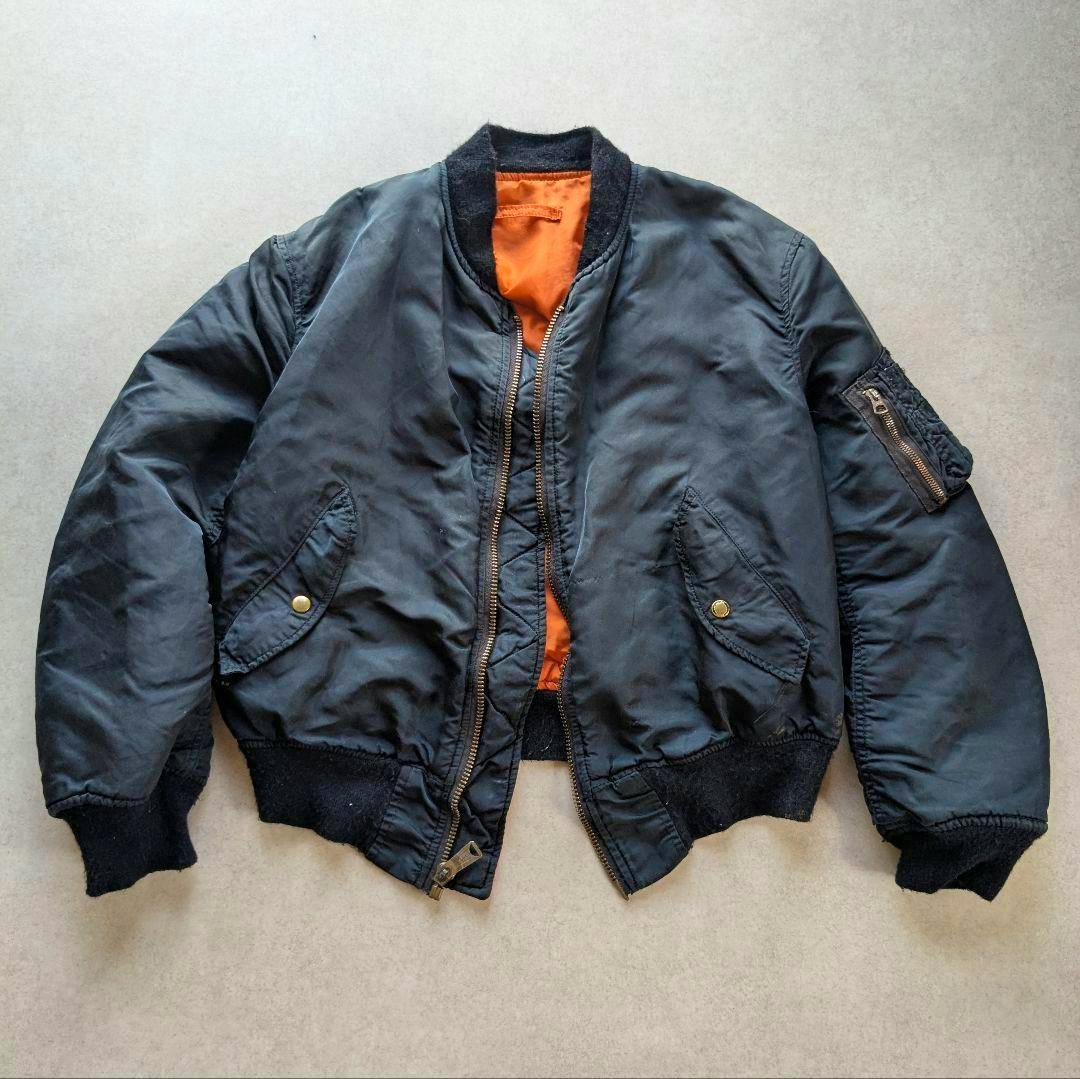 Front view of a black Alpha Industries MA-1 bomber jacket with orange lining laid flat.